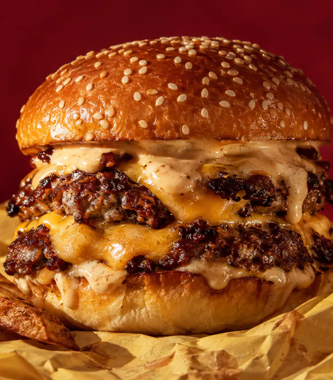 Hamburguesa doble con salsa y papas rústicas sobre papel madera (imagen ilustrativa).